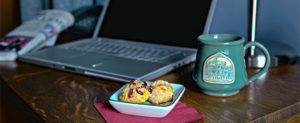 Laptop at workspace with Ash Street Inn coffee mug and scones