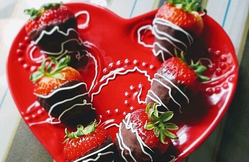Decorative red plate with six strawberries covered in dark and white chocolate.