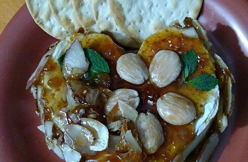 Red plate showing round crackers and fruit and honey on white cheese.