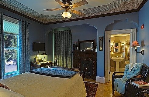 Bedroom with blue walls, arched doorways. decorative ceiling with fan and dark brown furniture.