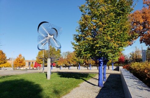 Grassy area showing tree with blue trunks surrounding a tall decorative metal sculpture.