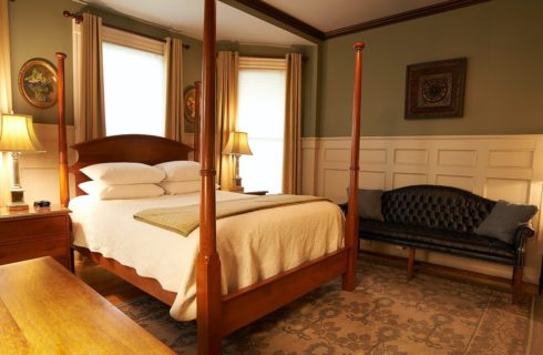 Large bedroom with wooden four poster bed, large rug, board and batten on walls and a leather couch