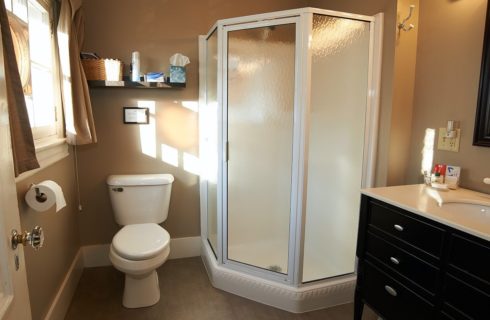 Bathroom with beige walls, black and white vanity, toilet and corner stand up shower.