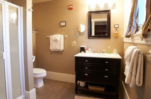 Bathroom with black and white vanity, white toilet, white towels on silver racks, and stand up shower.