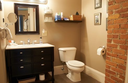 Bathroom with rectangular mirror over black and white vanity, white toilet and red brick corner feature.