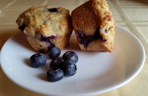 Circular white plate holding two freshly baked blueberry muffins and six little blueberries.