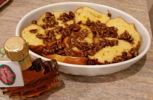 White oval plate of french toast with chopped walnuts and bottle of pure maple syrup on the table.