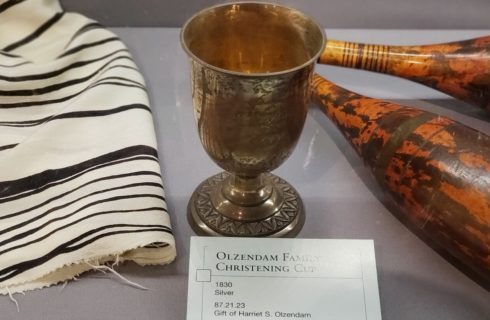 Museum case displaying a golden goblet, brown wooden artifacts and cream and black material