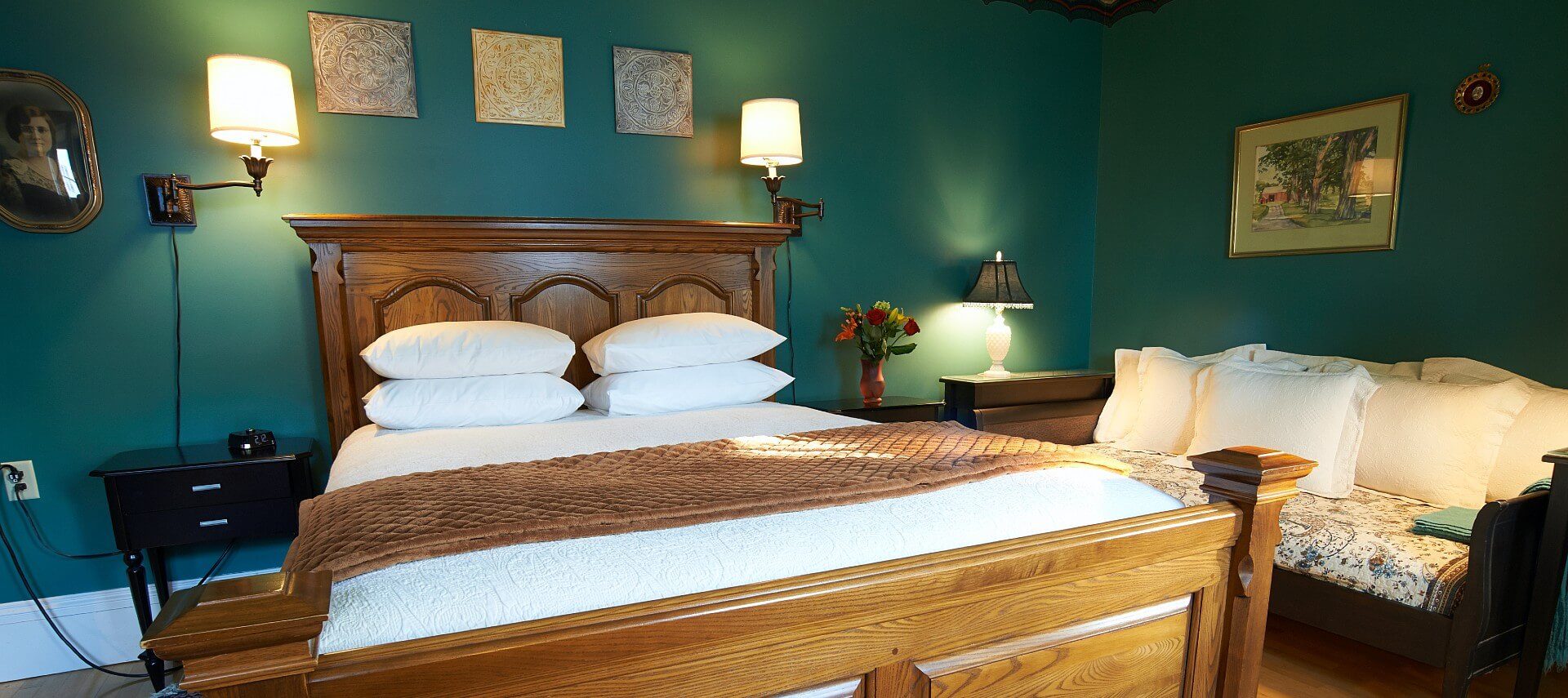 Bedroom with green walls, queen bed with large wooden headboard and footboard, day bed and paintings on the walls.