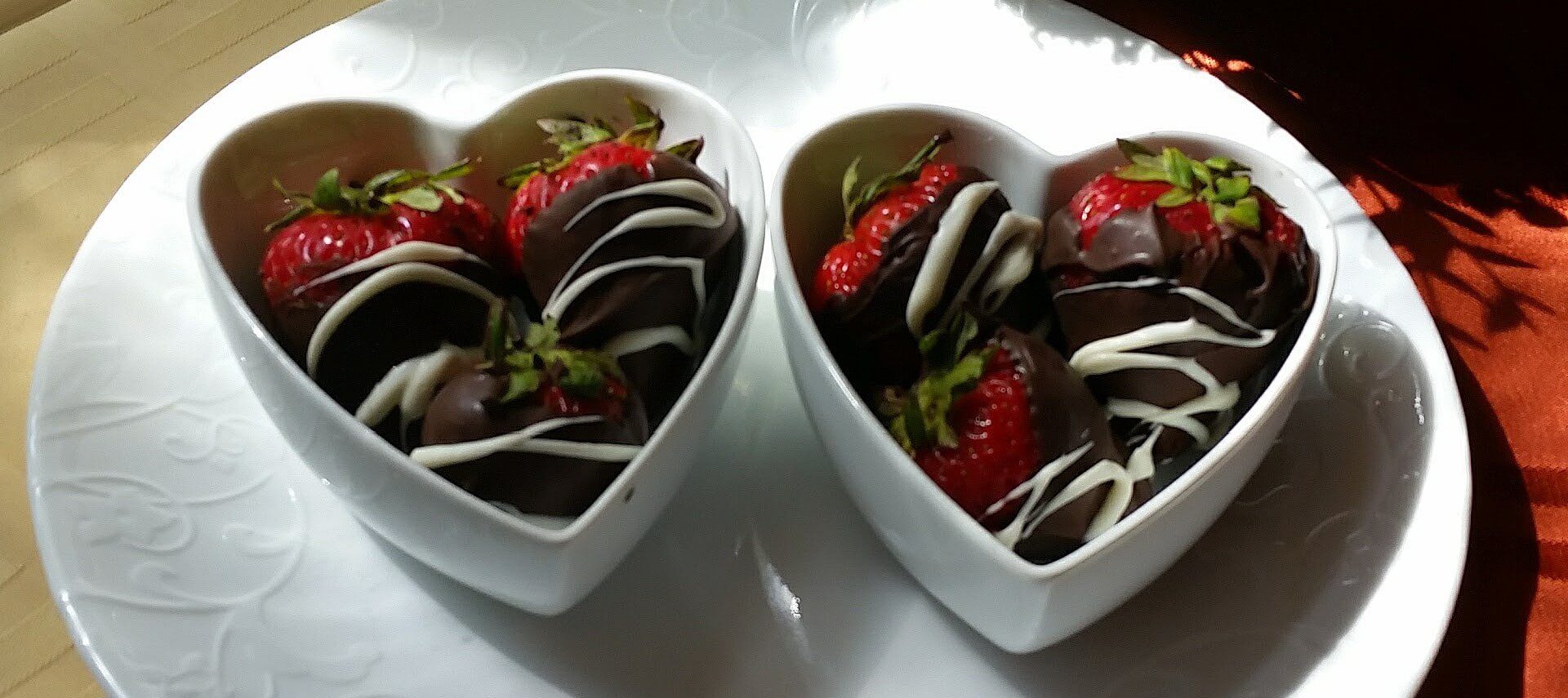 Two white heart-shaped bowls holding strawberries covered in dark and white chocolate.