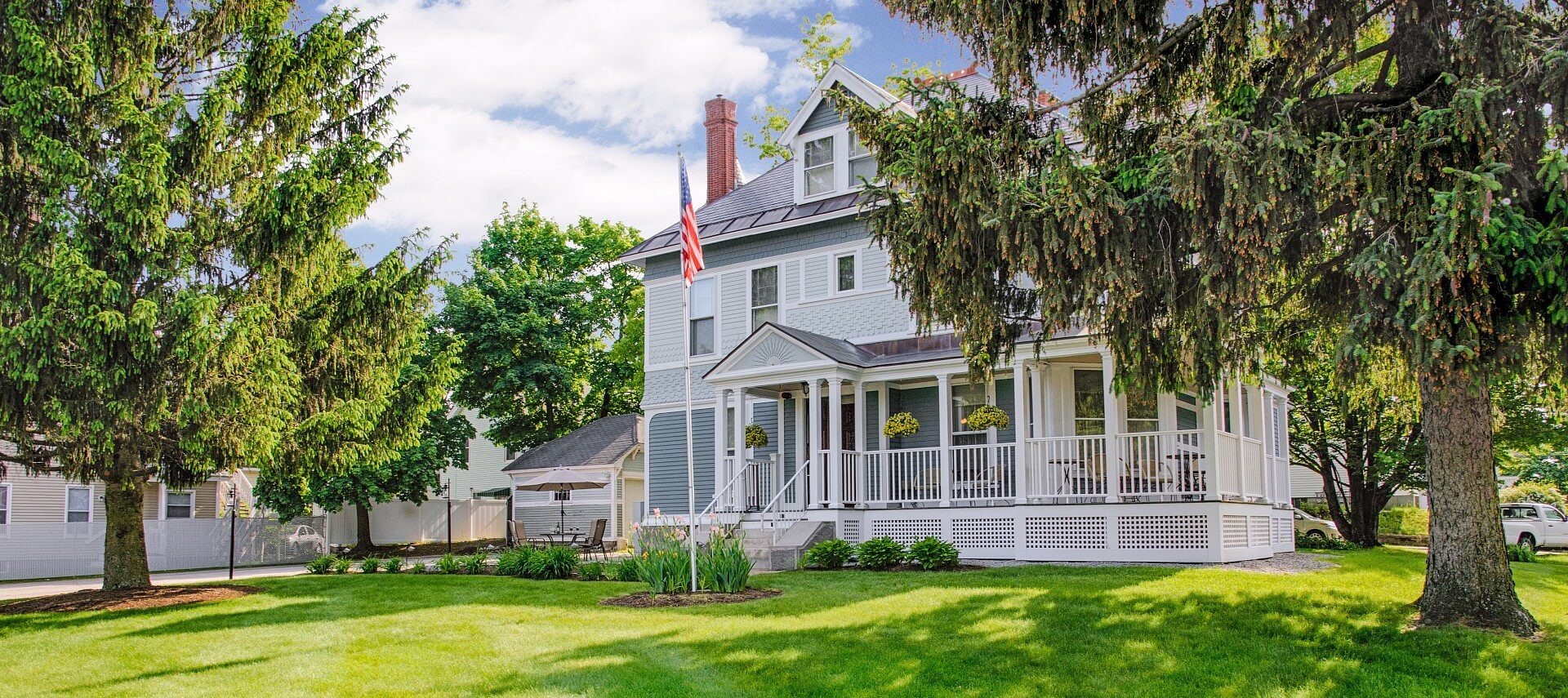 Front a large, two story home in grey siding, with white trim and large white wrap around porch.