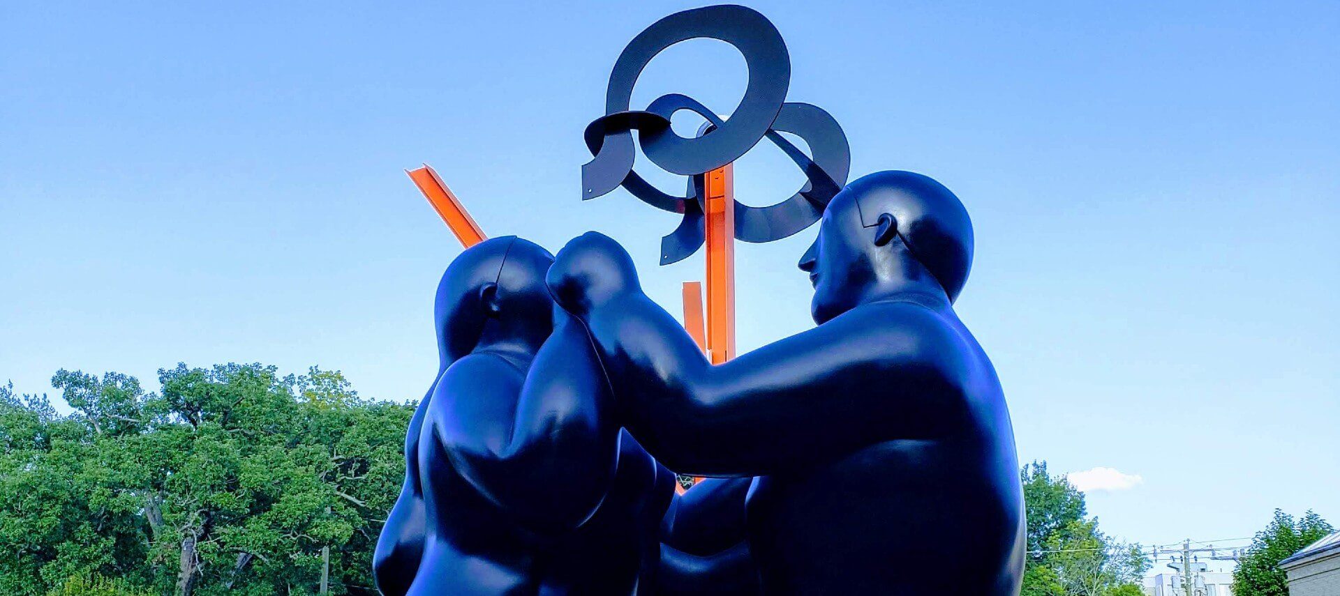 Large artistic sculpture depicting two people facing each other holding hands with orange spikes and circular designs above.