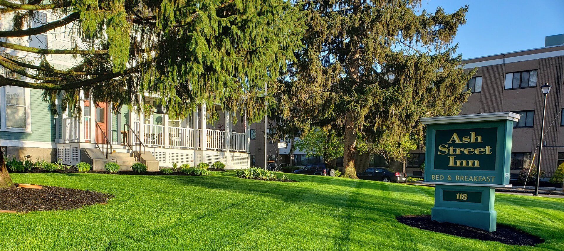 Home with grey-blue siding and porch with white railing next to large grassy area with sign for an inn.