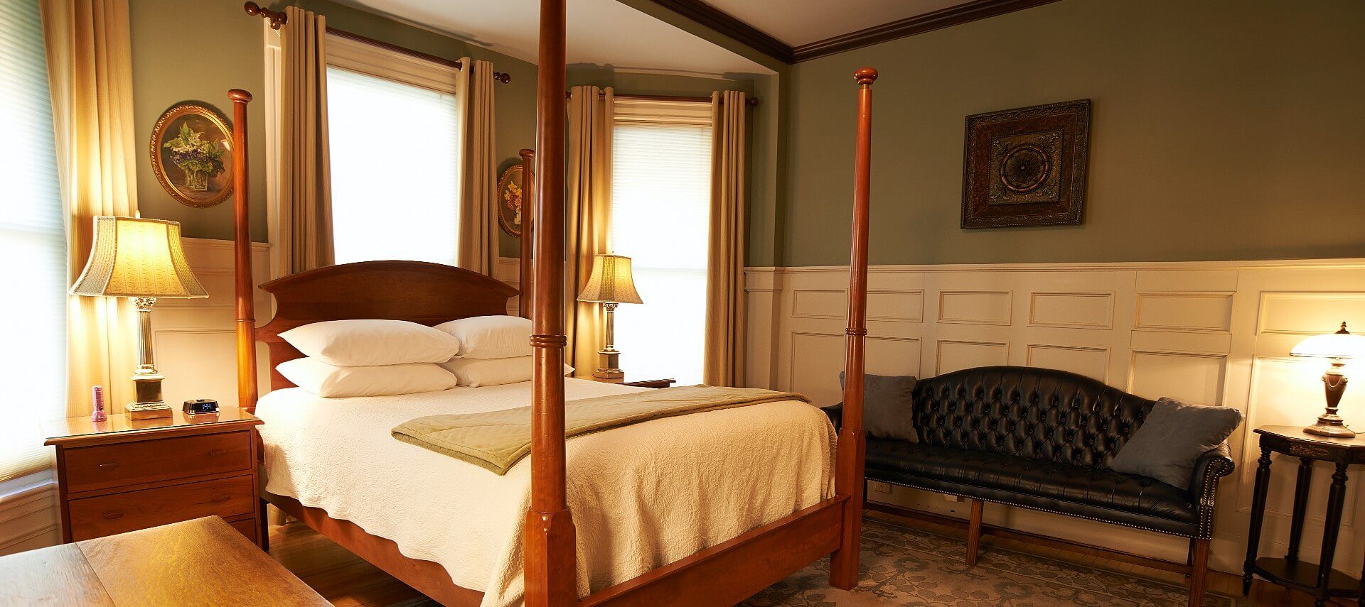 Elegant guest room with a four poster bed, black leather couch, and board and batten feature on the walls