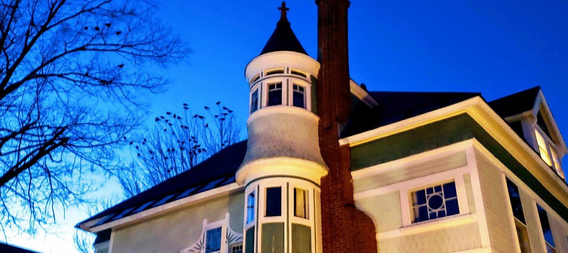 Top corner view of a home featuring red brick fireplace and dome with spire top against a blue sky at dusk