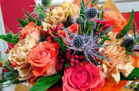 Gorgeous bouquet of flowers with red, orange and yellow roses, and purple and green accents.