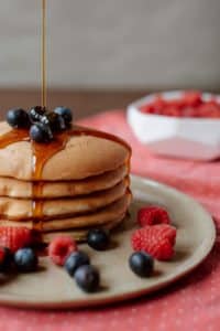 syrup dripping onto a stack of pancakes surrounded by blueberries and raspberries