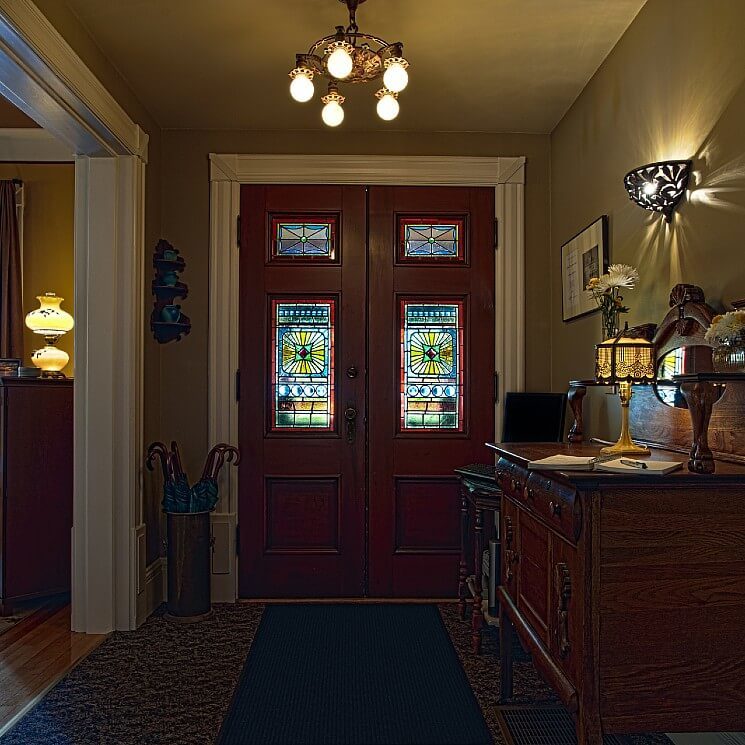 Large dark brown front doors with stained glass windows and the foyer of a home with antique furniture.